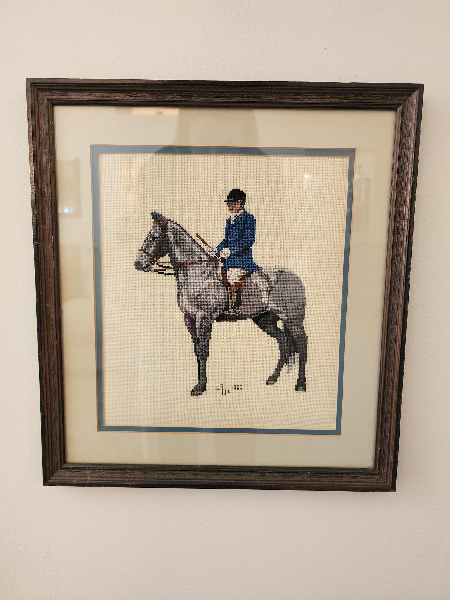 Charming framed needlepoint (or cross-stitch) artwork capturing a classic equestrian scene, signed and dated 1985.