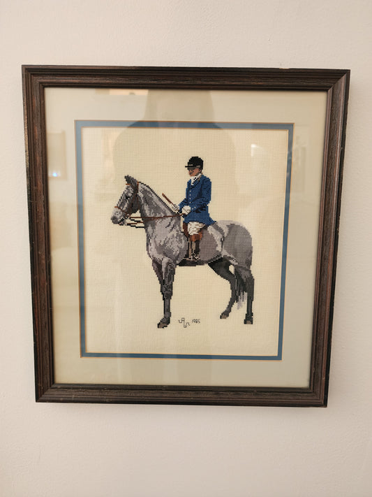 Charming framed needlepoint (or cross-stitch) artwork capturing a classic equestrian scene, signed and dated 1985.