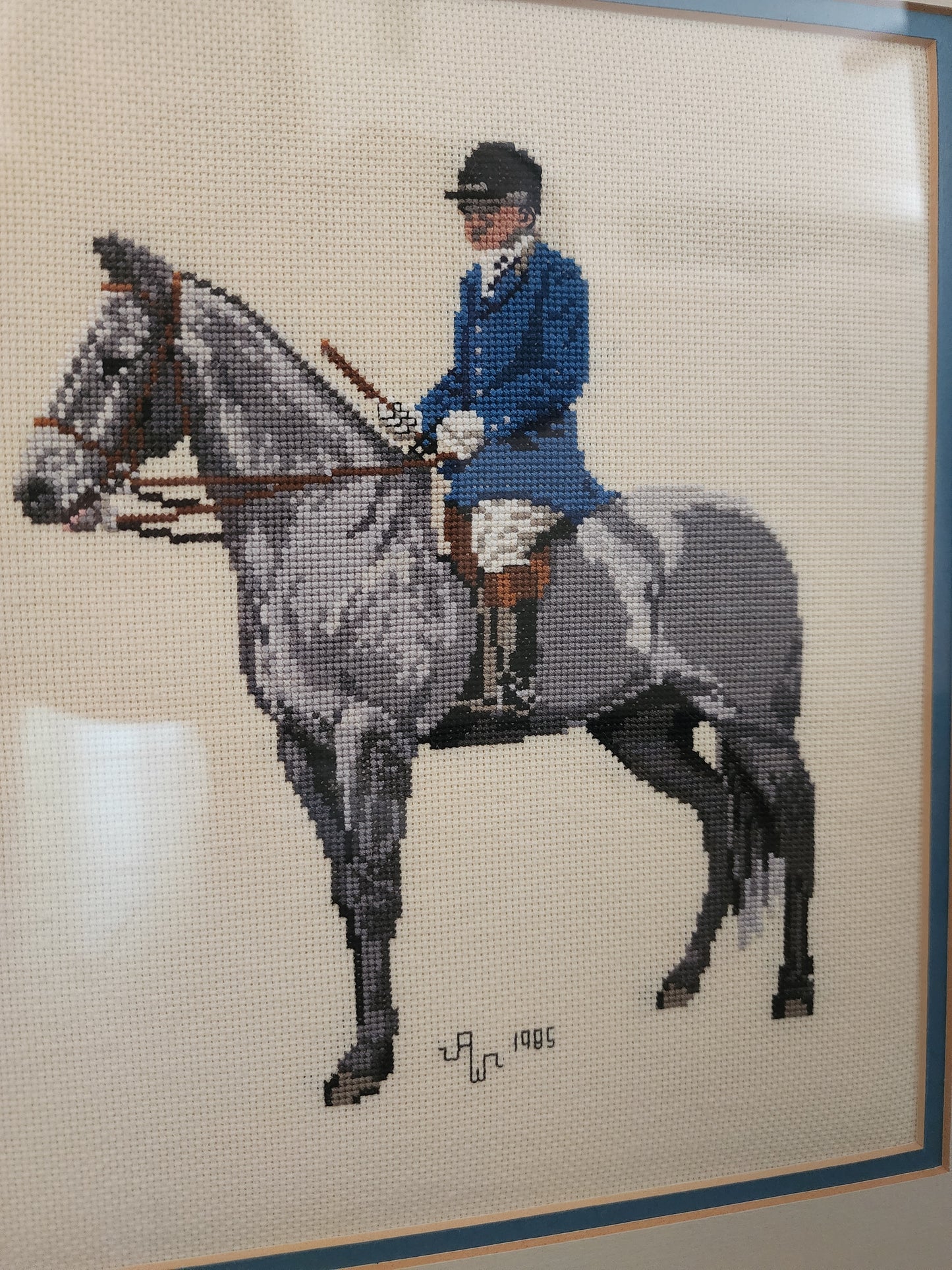 Charming framed needlepoint (or cross-stitch) artwork capturing a classic equestrian scene, signed and dated 1985.